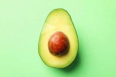 Photo of Half of fresh avocado on green background, top view