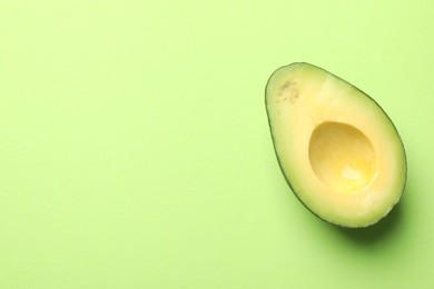 Photo of Half of fresh avocado on light green background, top view. Space for text