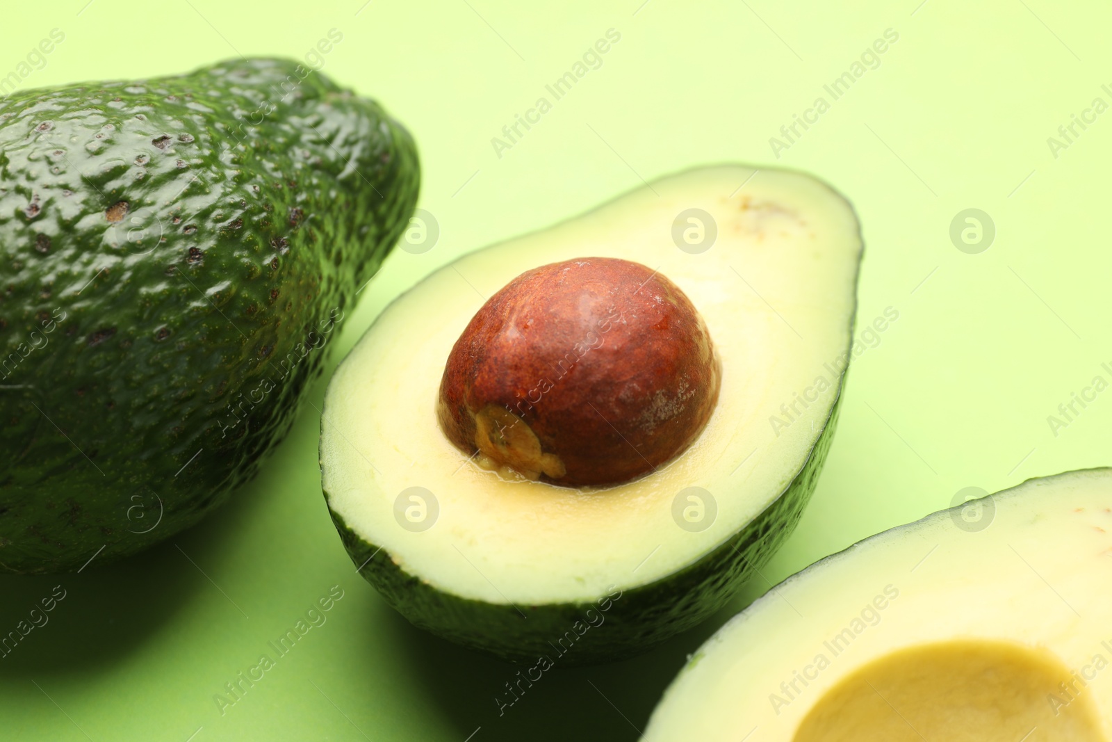 Photo of Whole and cut avocados on light green background, closeup