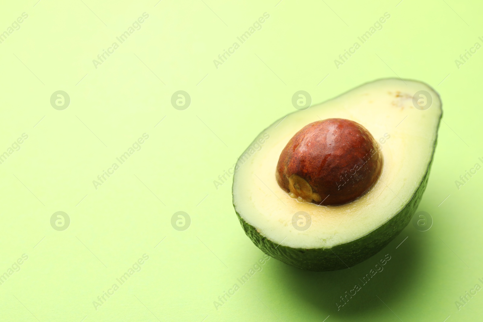 Photo of Half of fresh avocado on light green background, closeup. Space for text