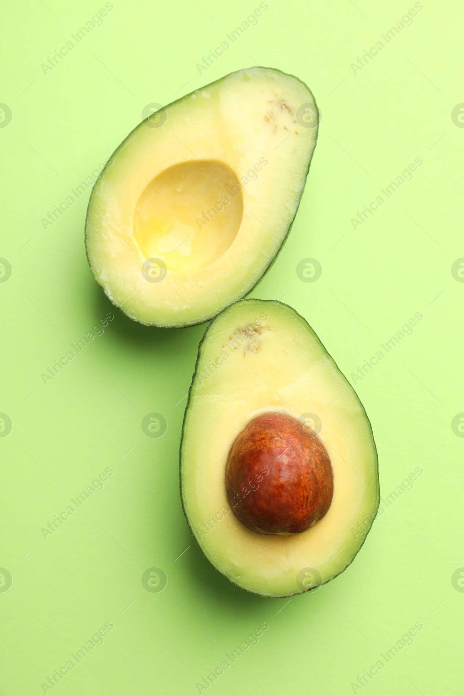 Photo of Halves of fresh avocado on light green background, flat lay