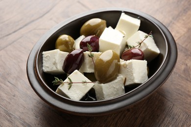 Photo of Marinated olives with feta cheese and rosemary on wooden table, closeup