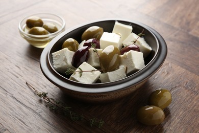 Photo of Marinated olives with feta cheese and rosemary on wooden table, closeup