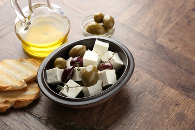 Photo of Marinated olives with feta cheese, bread pieces, oil and rosemary on wooden table, closeup. Space for text