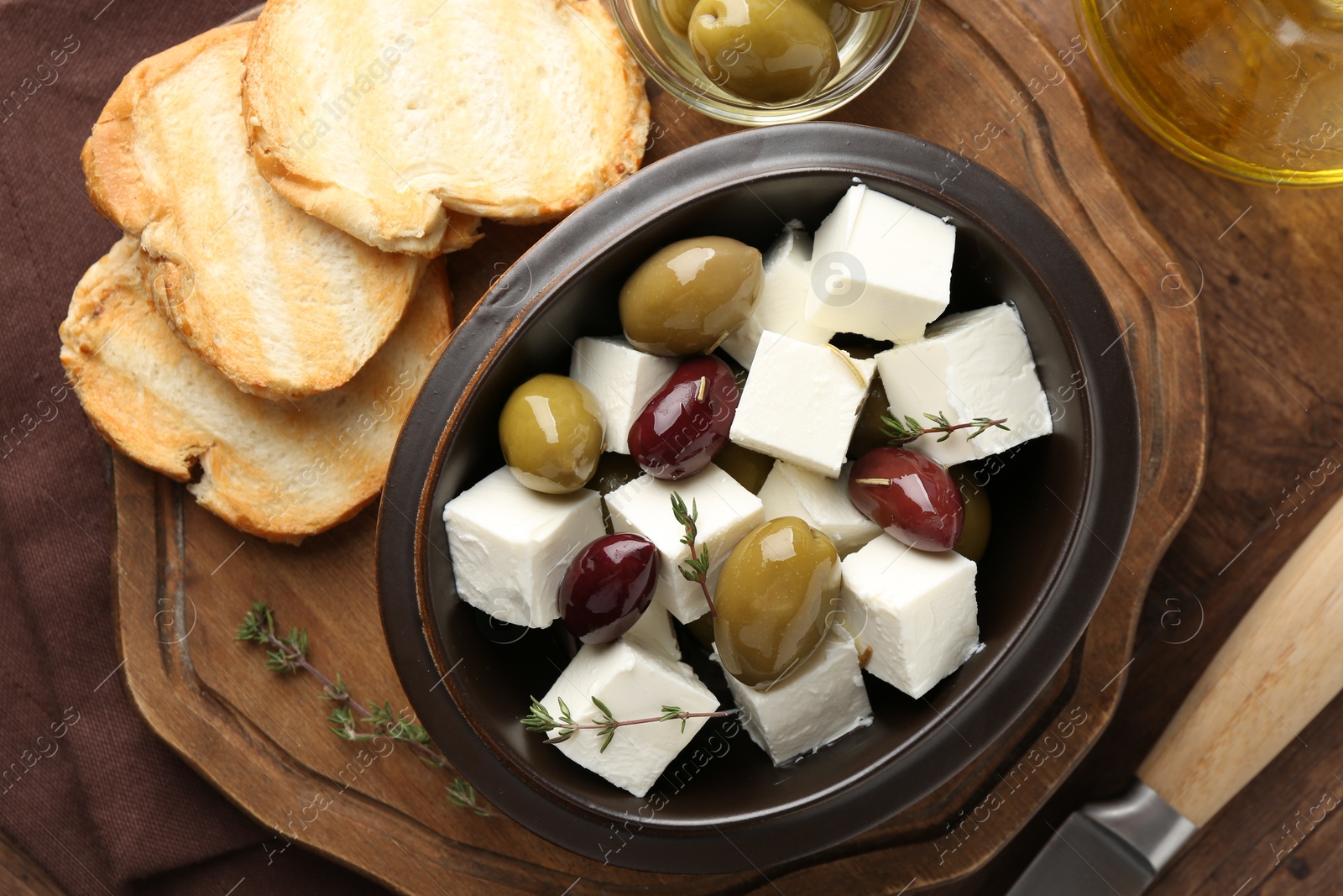 Photo of Marinated olives with feta cheese, bread pieces, oil and rosemary on table, flat lay