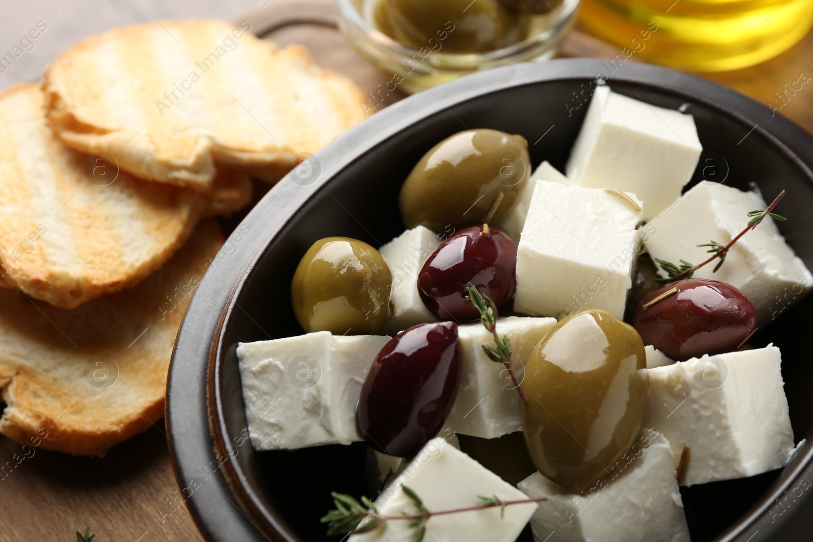 Photo of Marinated olives with feta cheese, rosemary and bread pieces on table, closeup