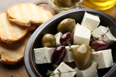 Photo of Marinated olives with feta cheese, rosemary and bread pieces on table, closeup