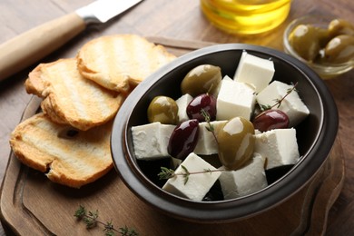 Photo of Marinated olives with feta cheese, bread pieces, oil and rosemary on table, closeup