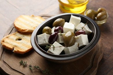 Photo of Marinated olives with feta cheese, bread pieces, oil and rosemary on table, closeup