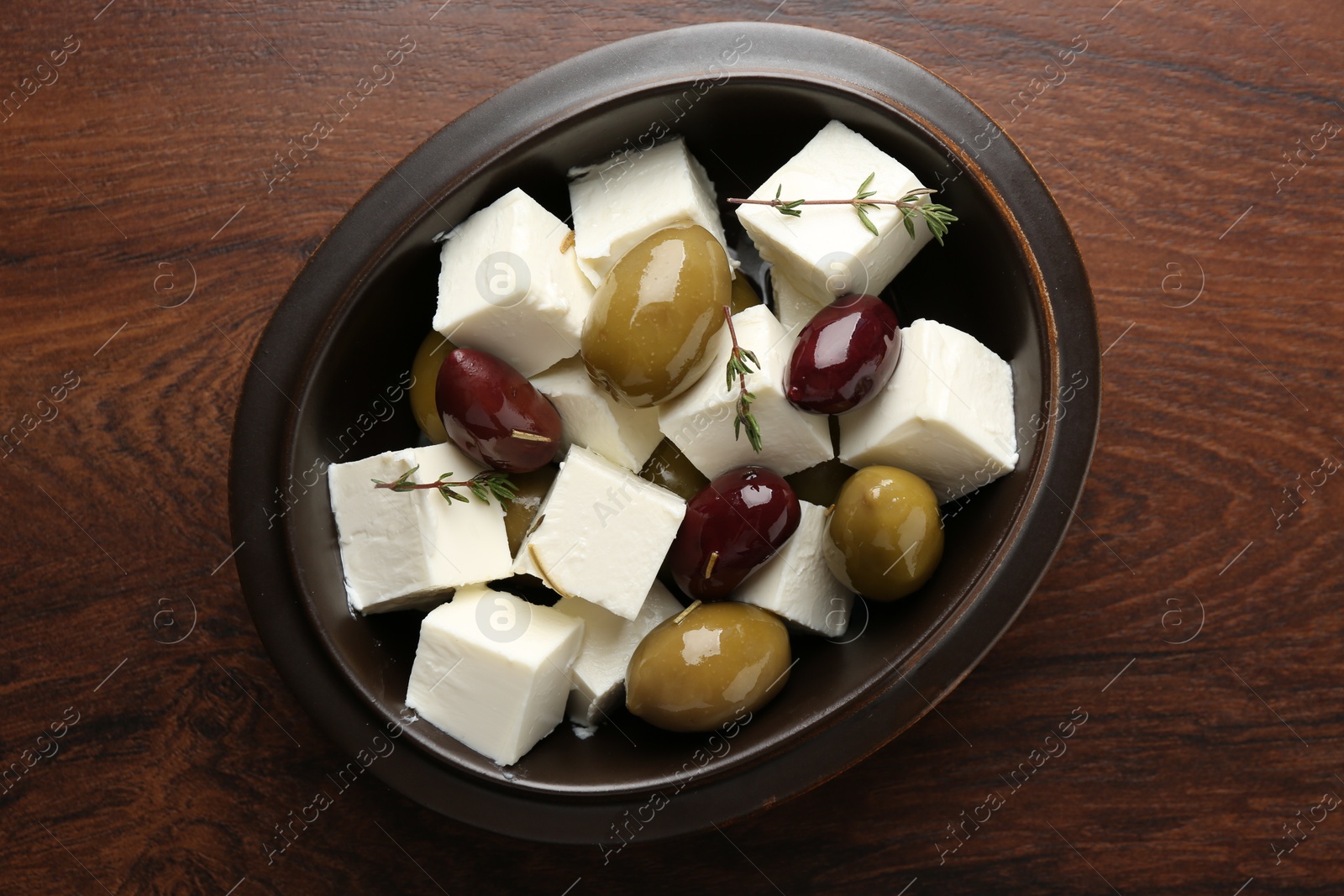 Photo of Marinated olives with feta cheese and rosemary on wooden table, top view