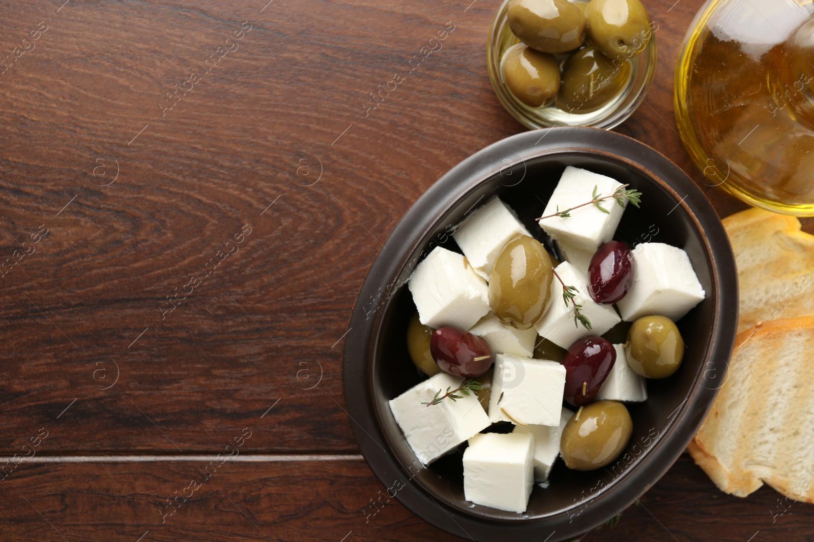 Photo of Marinated olives with feta cheese, bread pieces, oil and rosemary on wooden table, flat lay. Space for text