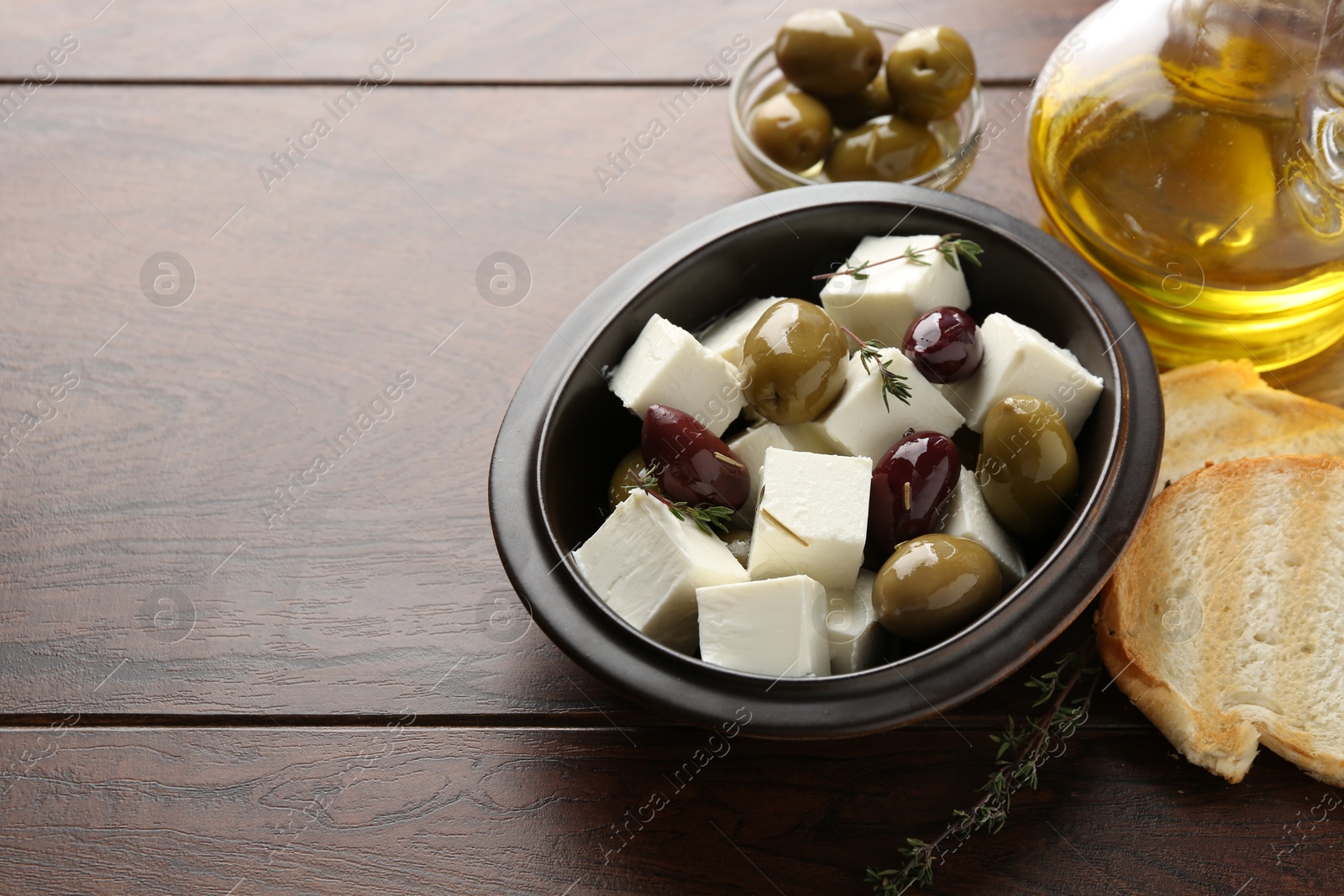 Photo of Marinated olives with feta cheese, bread pieces, oil and rosemary on wooden table, closeup. Space for text