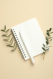 Notebook, pen and green twigs on beige background, flat lay