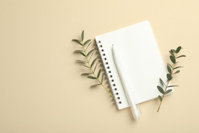 Notebook, pen and green twigs on beige background, flat lay. Space for text