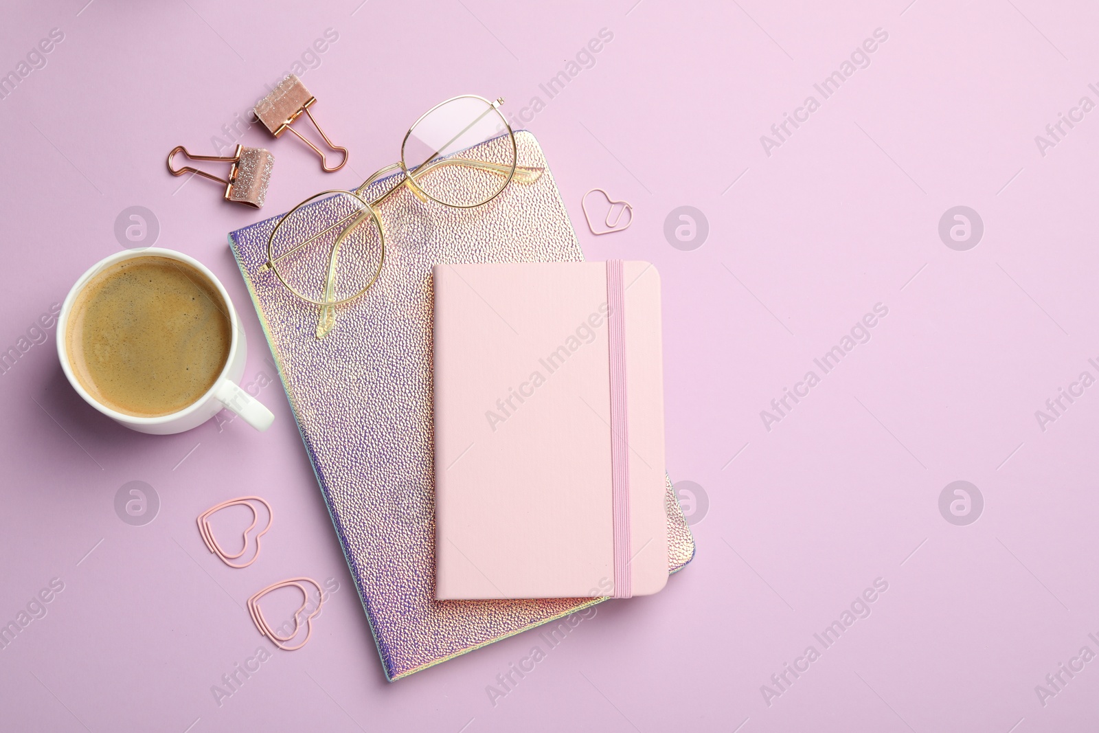 Photo of Paper clips, other different stationery, glasses and coffee on lilac background, flat lay. Space for text