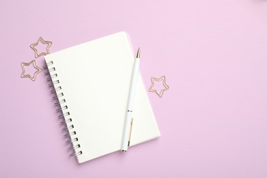 Star shaped paper clips, notebook and pen on lilac background, flat lay. Space for text