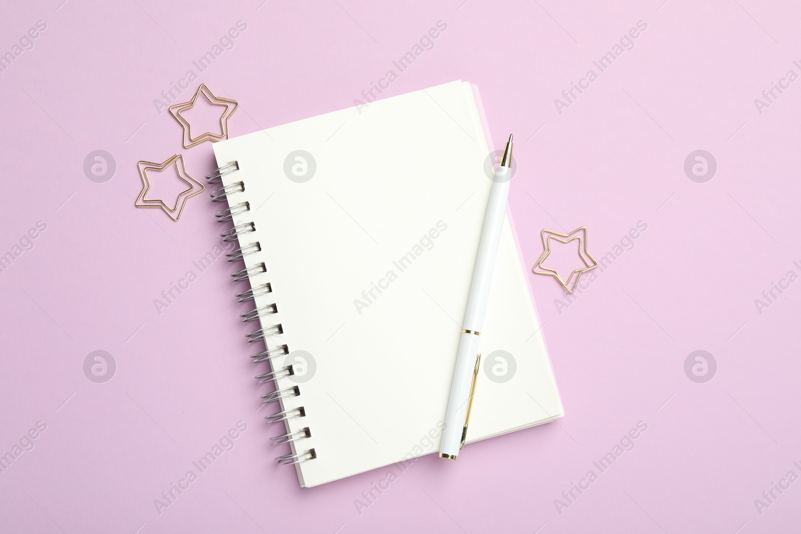 Photo of Star shaped paper clips, notebook and pen on lilac background, flat lay