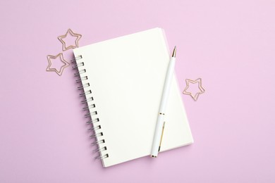 Star shaped paper clips, notebook and pen on lilac background, flat lay