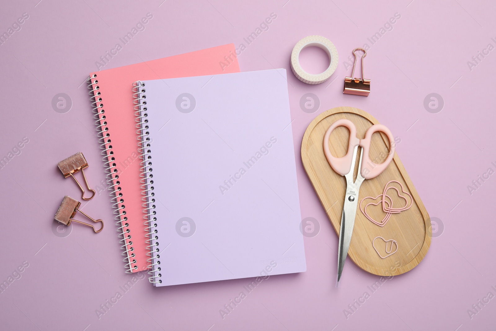 Photo of Paper clips and other different stationery on lilac background, flat lay