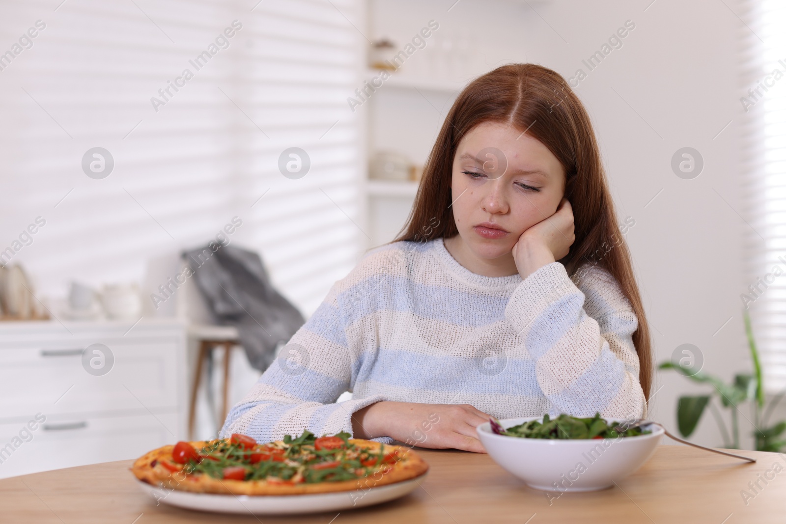 Photo of Sad teenage girl with pizza and bowl of salad at wooden table. Eating disorder