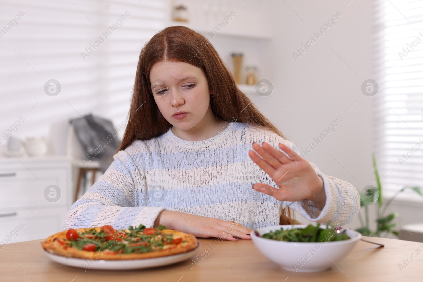 Photo of Sad teenage girl with pizza and bowl of salad at wooden table. Eating disorder