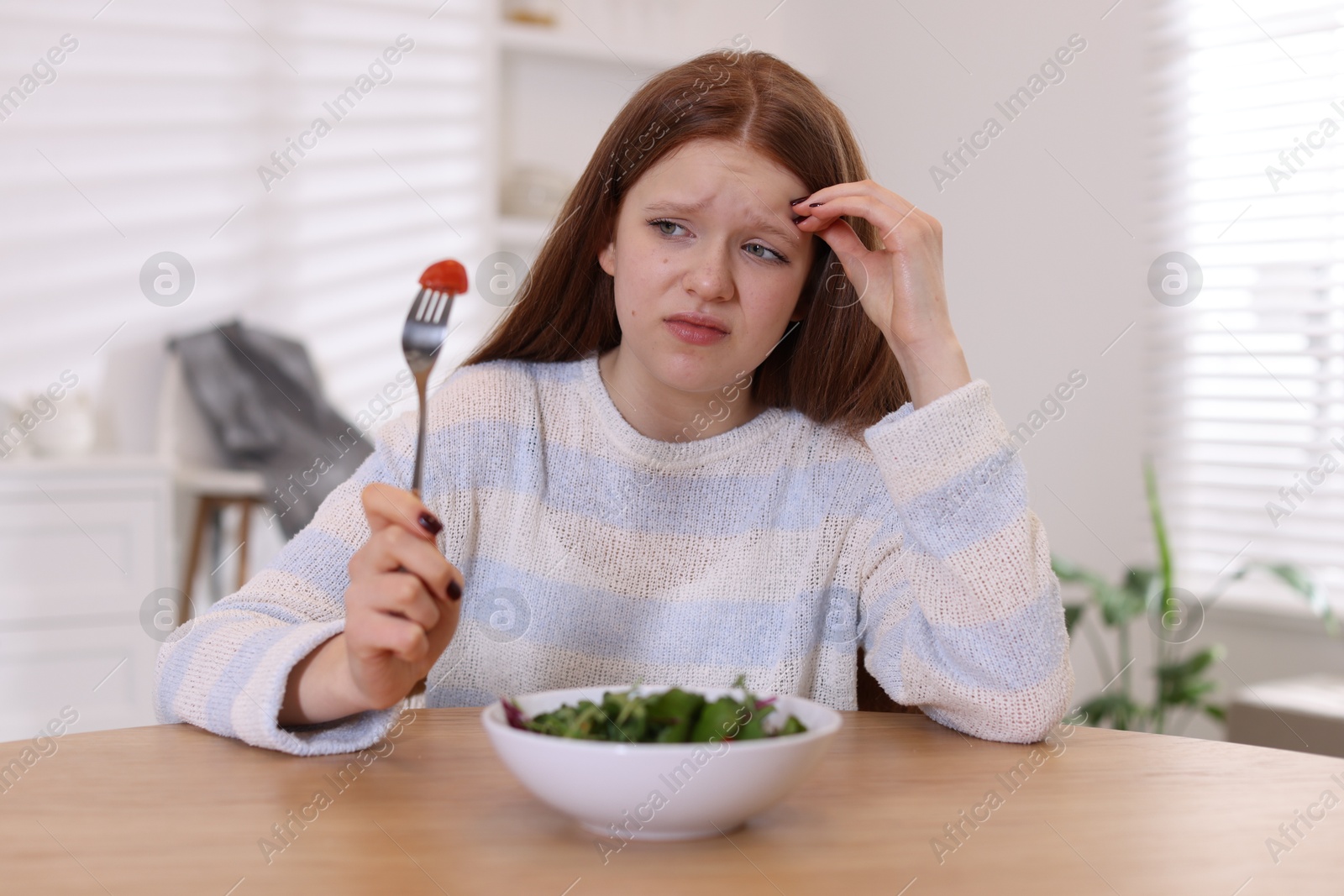 Photo of Sad teenage girl with bowl of salad at wooden table. Eating disorder