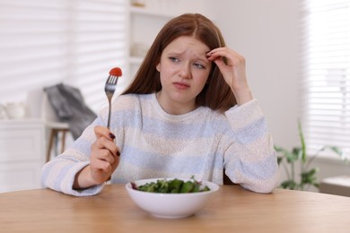 Photo of Sad teenage girl with bowl of salad at wooden table. Eating disorder