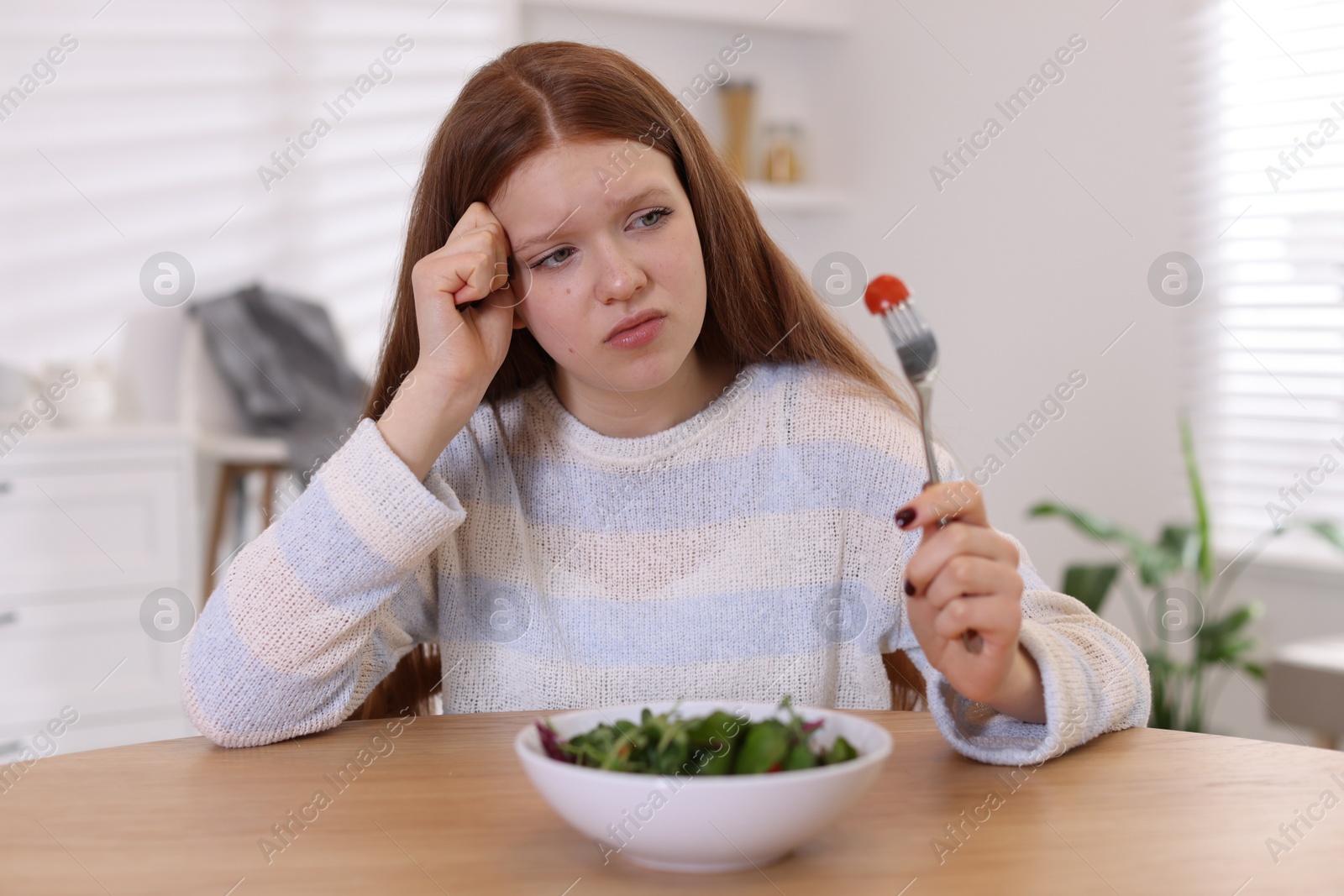 Photo of Sad teenage girl with bowl of salad at wooden table. Eating disorder