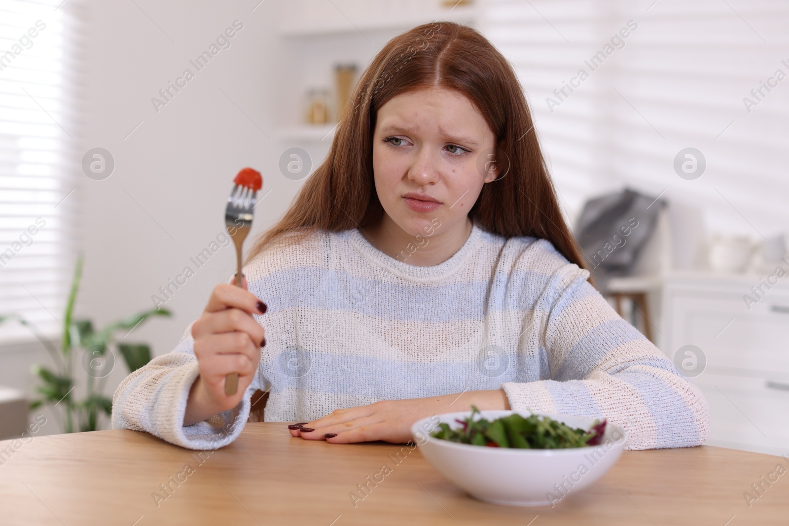 Photo of Sad teenage girl with bowl of salad at wooden table. Eating disorder