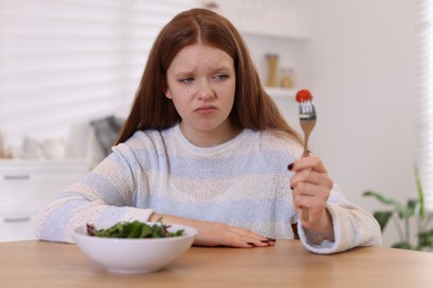 Photo of Sad teenage girl with bowl of salad at wooden table. Eating disorder