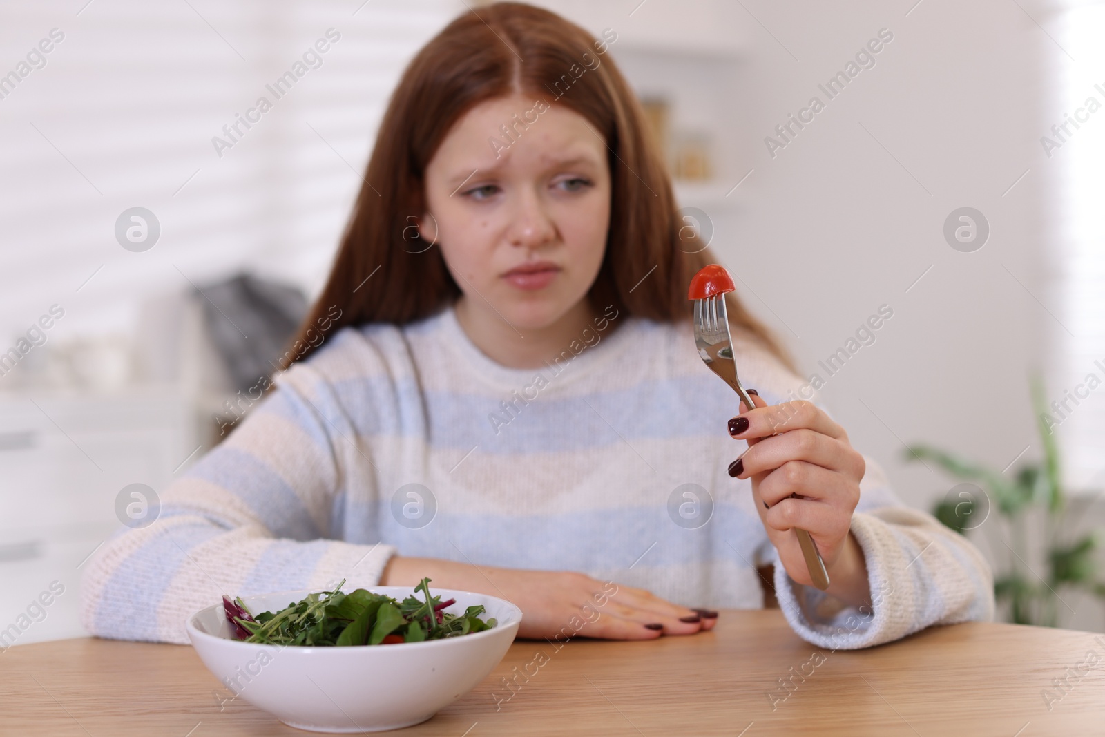 Photo of Sad teenage girl with bowl of salad at wooden table, selective focus. Eating disorder