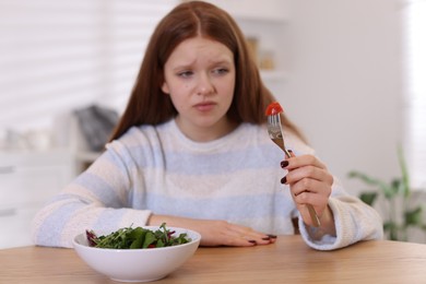 Sad teenage girl with bowl of salad at wooden table, selective focus. Eating disorder