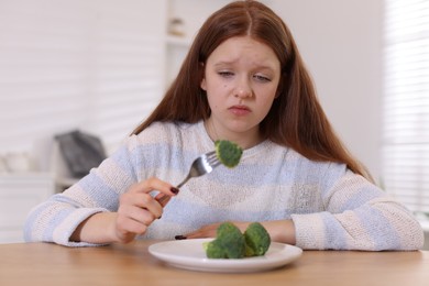 Photo of Sad teenage girl with broccoli at wooden table. Eating disorder