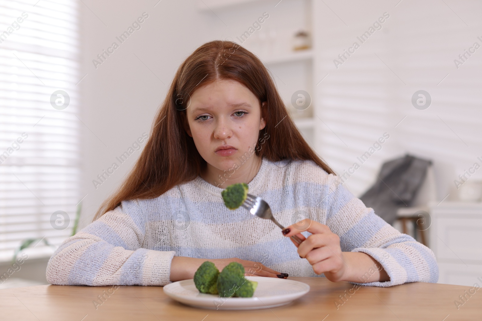 Photo of Sad teenage girl with broccoli at wooden table. Eating disorder