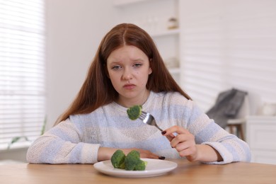 Photo of Sad teenage girl with broccoli at wooden table. Eating disorder