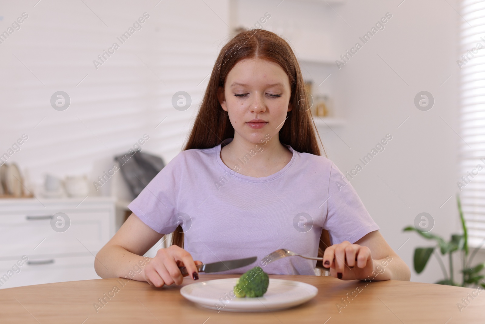 Photo of Sad teenage girl with broccoli at wooden table. Eating disorder