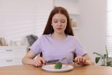 Photo of Sad teenage girl with broccoli at wooden table. Eating disorder