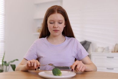 Photo of Sad teenage girl with broccoli at wooden table. Eating disorder