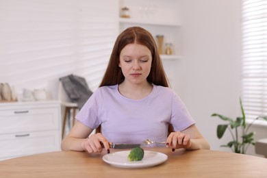 Photo of Sad teenage girl with broccoli at wooden table. Eating disorder