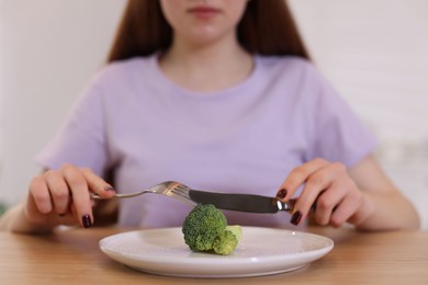 Photo of Teenage girl with broccoli at wooden table, closeup. Eating disorder