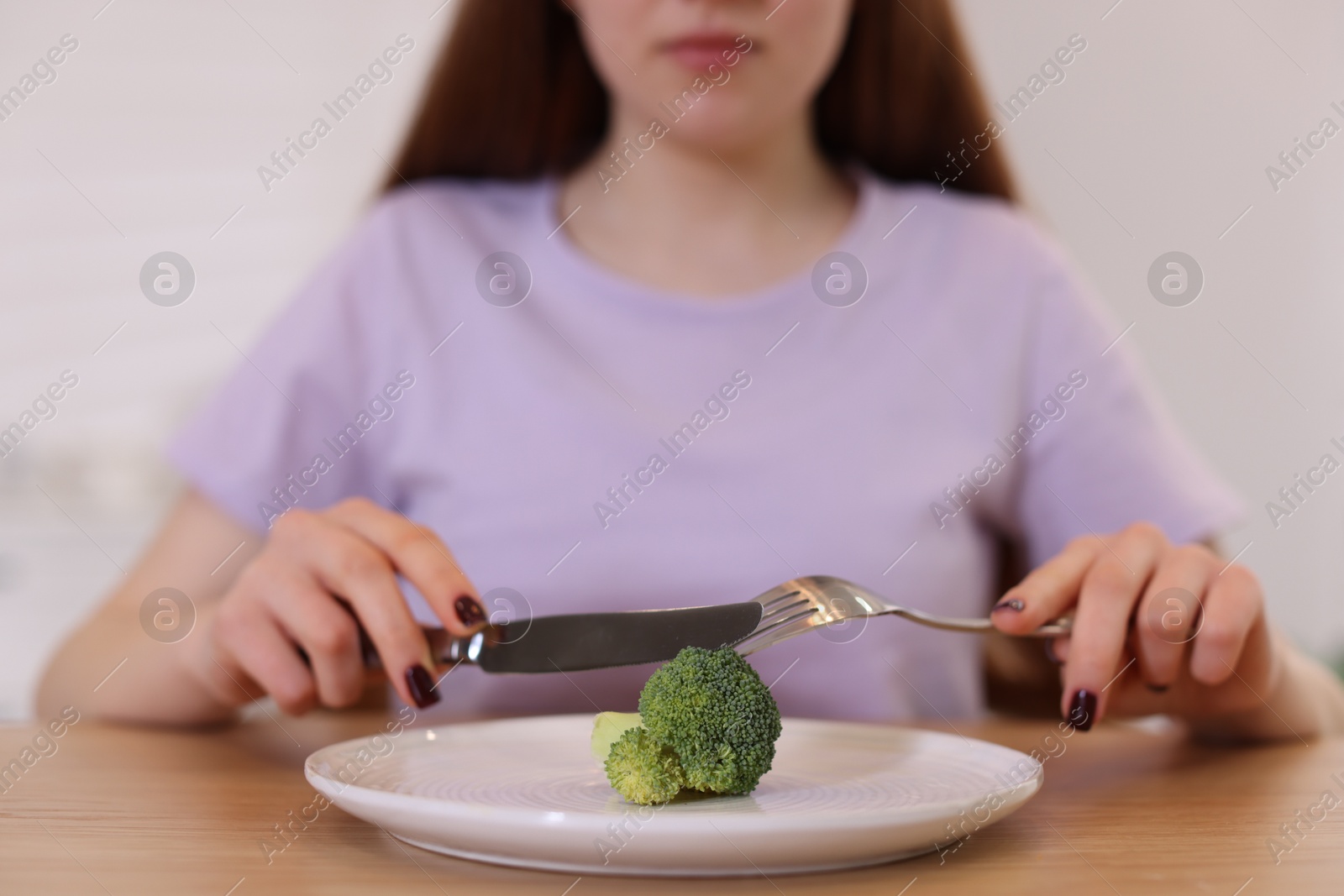 Photo of Teenage girl with broccoli at wooden table, closeup. Eating disorder