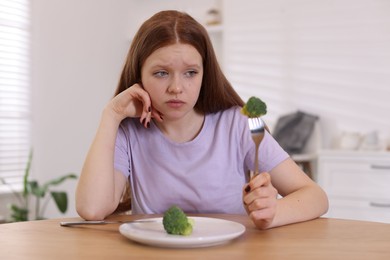 Photo of Sad teenage girl with broccoli at wooden table. Eating disorder