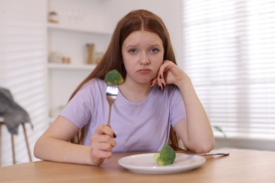 Photo of Sad teenage girl with broccoli at wooden table. Eating disorder