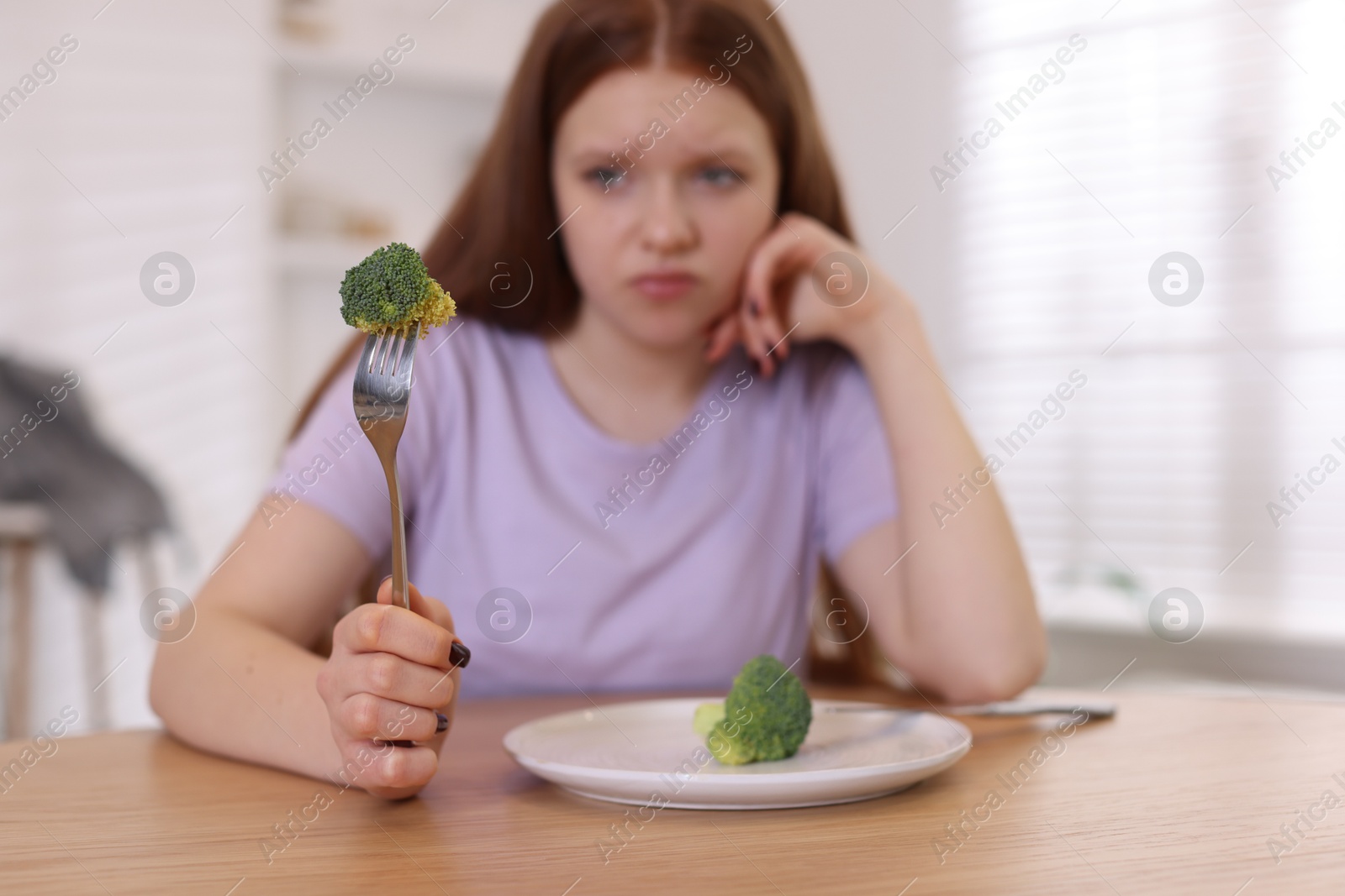 Photo of Sad teenage girl with broccoli at wooden table, selective focus. Eating disorder