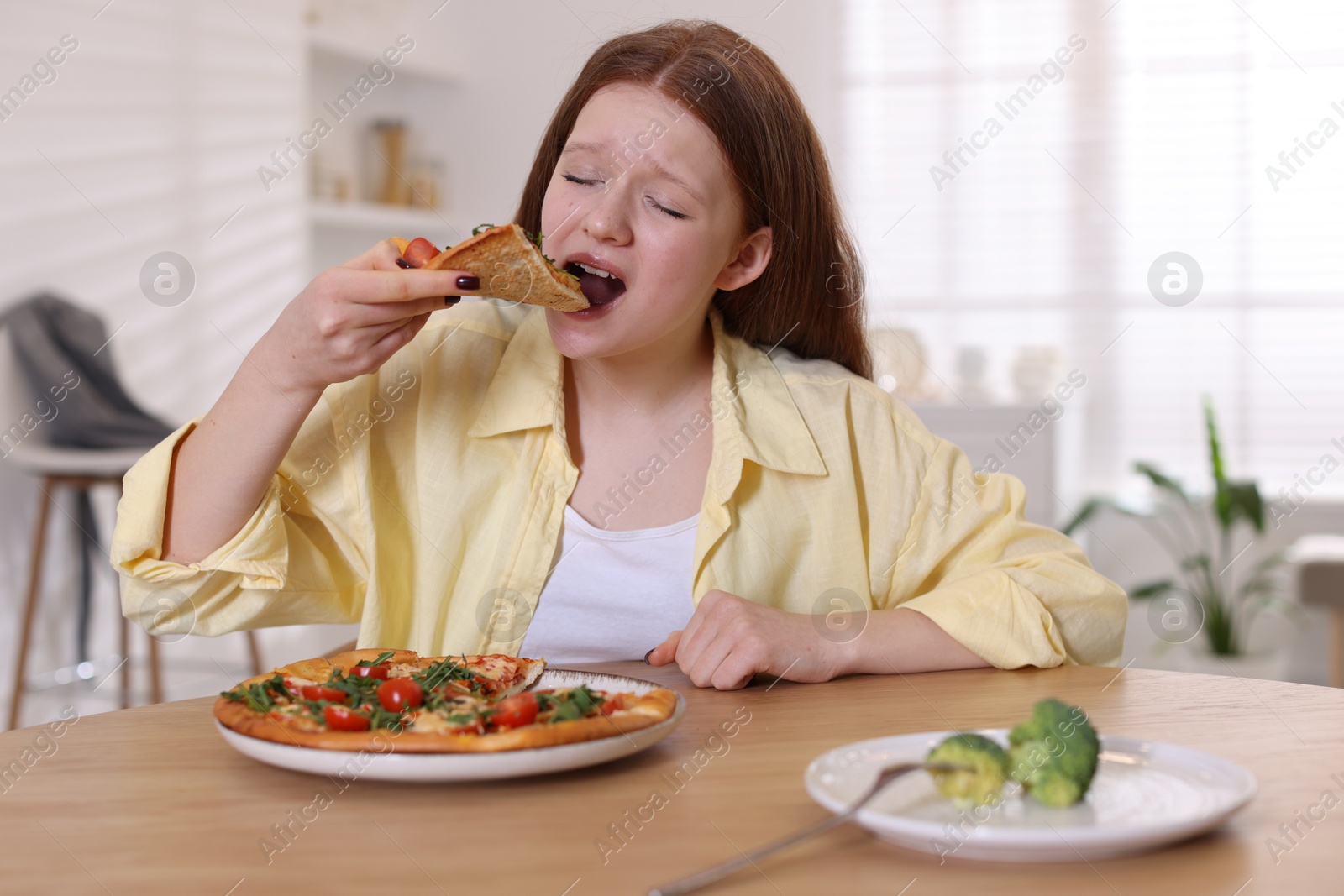 Photo of Sad teenage girl with piece of pizza at wooden table indoors. Eating disorder