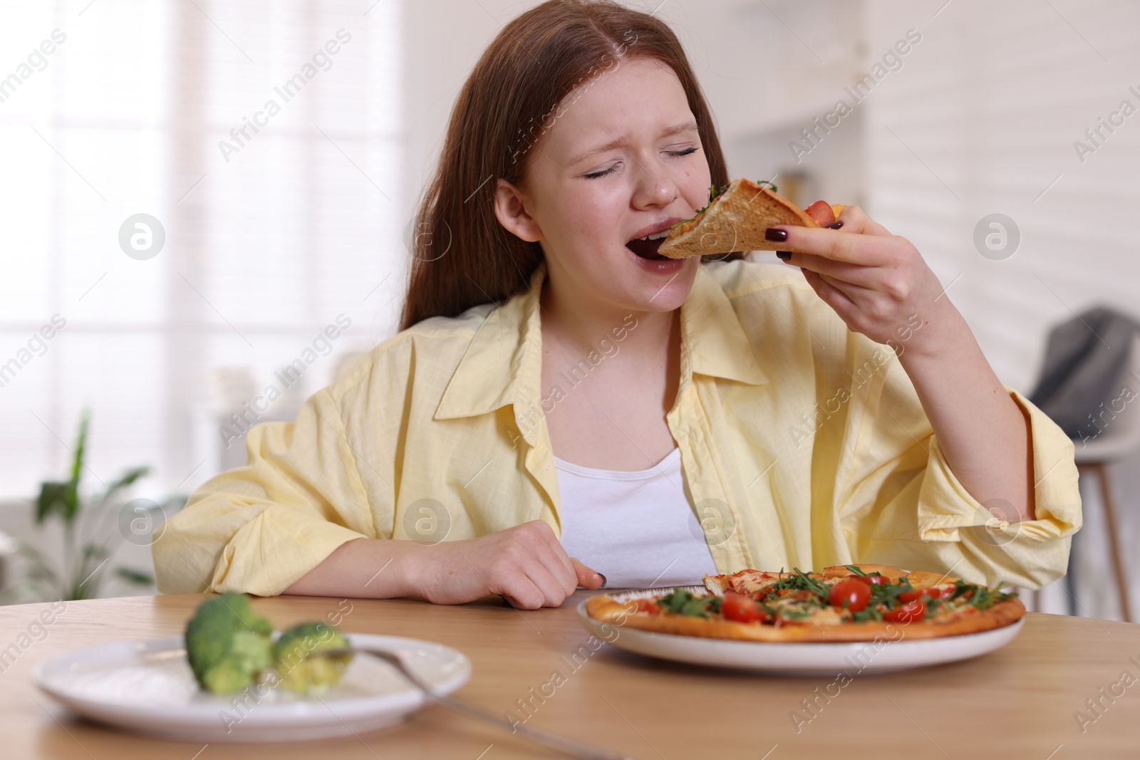 Photo of Sad teenage girl with piece of pizza at wooden table indoors. Eating disorder