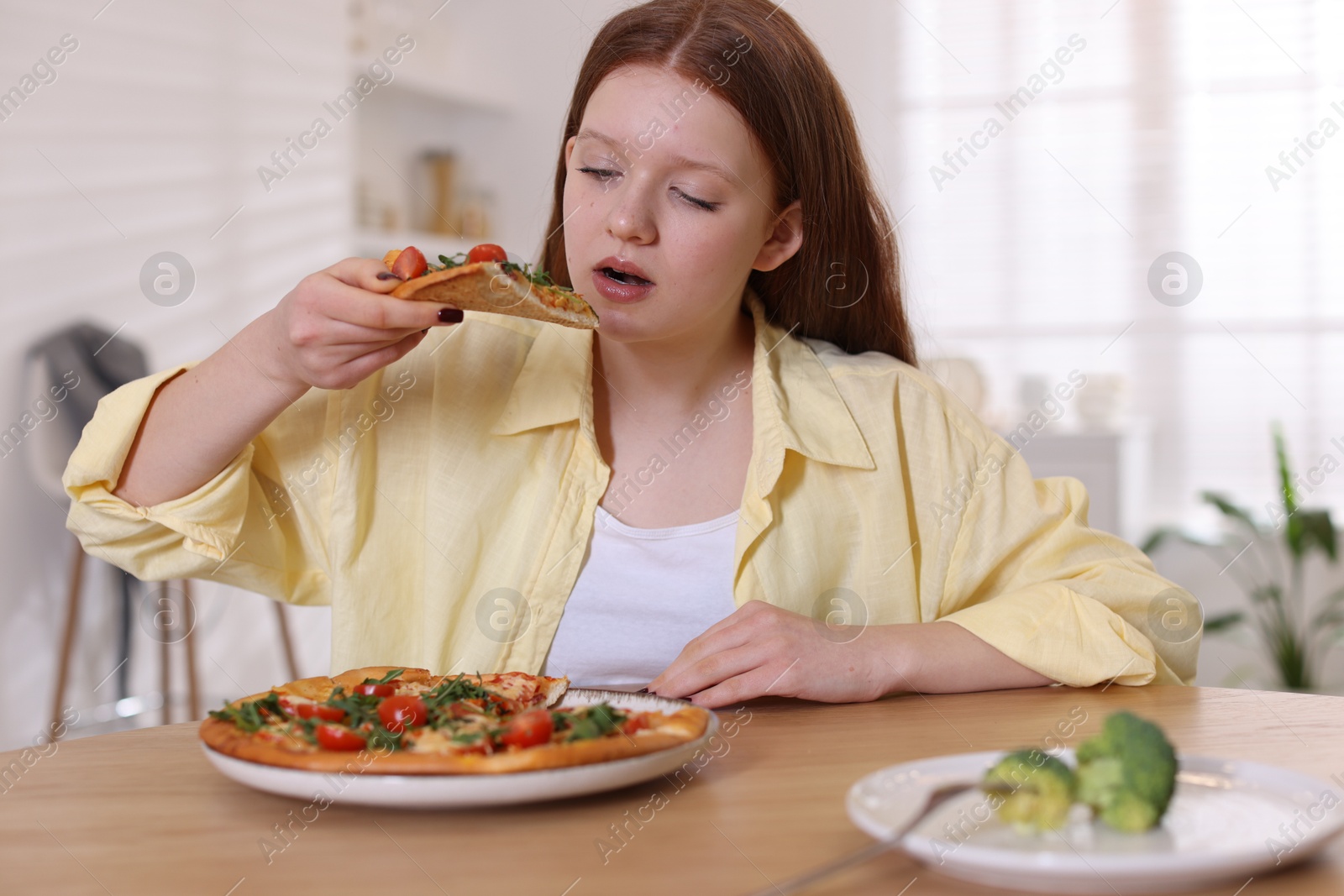 Photo of Sad teenage girl with piece of pizza at wooden table indoors. Eating disorder