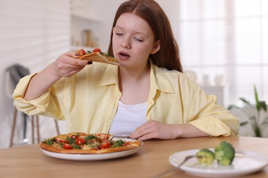 Photo of Sad teenage girl with piece of pizza at wooden table indoors. Eating disorder