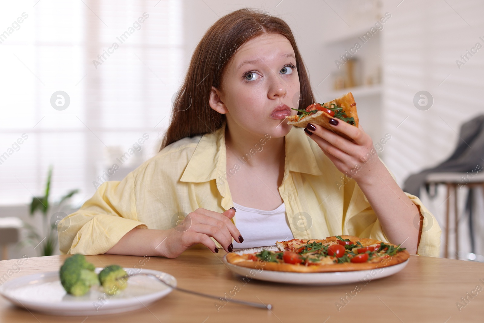 Photo of Sad teenage girl with piece of pizza at wooden table indoors. Eating disorder