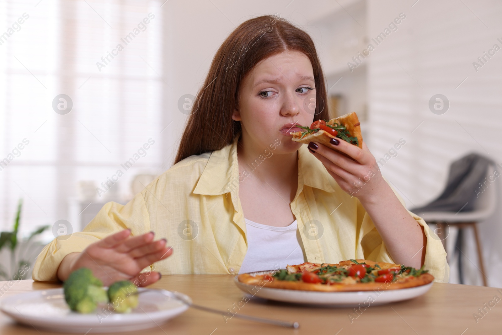 Photo of Sad teenage girl with piece of pizza at wooden table indoors. Eating disorder